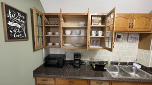 Een keuken met houten kastjes, een magnetron, een koffiezetapparaat en een spoelbak.