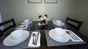 Een eettafel gedekt met witte borden, kommen, bestek en glazen, met een fles wijn en druiven op tafel.