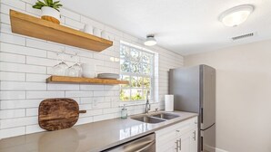 A modern kitchen with white subway tiles, wooden shelves, a stainless steel refrigerator, and a dishwasher. - Beechwood  Suites  A (Sarasota)