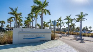 A sign for Siesta Beach, a Sarasota County park, with a paved walkway and palm trees in the background. - Beechwood  Suites  A (Sarasota)