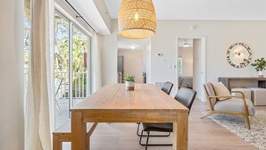 A spacious room with a large wooden table, black chairs, a woven pendant light, and a view of the outdoors through large windows. - Beechwood  Suites  A (Sarasota)