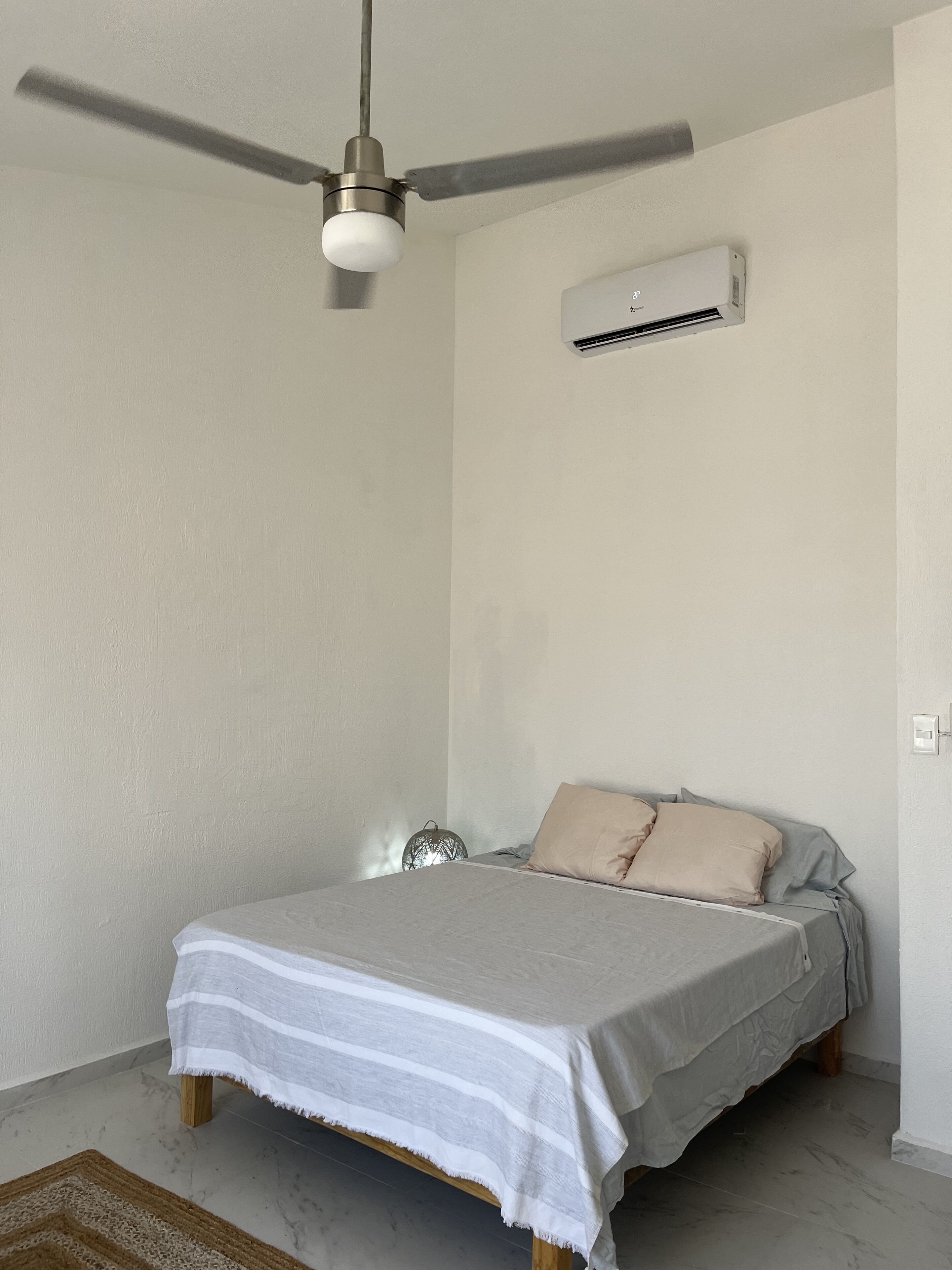 Ein Schlafzimmer mit einem Bett, einem Deckenventilator, einer Klimaanlage und einem kleinen Nachttisch.