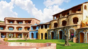 A courtyard with multiple buildings featuring arched windows and balconies, surrounded by well-maintained grass and trees. - Cozy apartment in Marinella (SS) with house sea view (Marinella (SS))