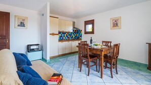 A living room with a sofa, a dining table with chairs, a kitchen with colorful tiles, and a window. - Lovely apartment in San Teodoro with WiFi (San Teodoro)