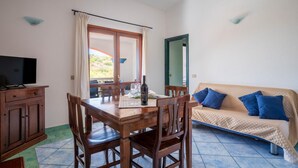 A dining area with a wooden table and chairs, a television on a cabinet, a sofa with blue cushions, and a view through a window. - Lovely apartment in San Teodoro with WiFi (San Teodoro)