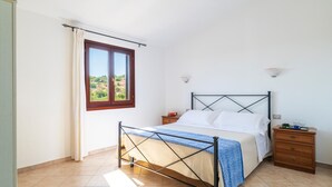 A bedroom with a bed, nightstands, a window with curtains, and a view of greenery outside. - Lovely apartment in San Teodoro with WiFi (San Teodoro)