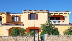 A two-story building with a yellow facade, red shutters, and a stone wall in front. - Lovely apartment in San Teodoro with WiFi (San Teodoro)