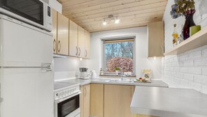 A modern kitchen with white appliances, wooden cabinets, a large window with a view of trees, and a brick wall backsplash. - 3 bedroom lovely home in Hurup Thy (Hurup Thy)