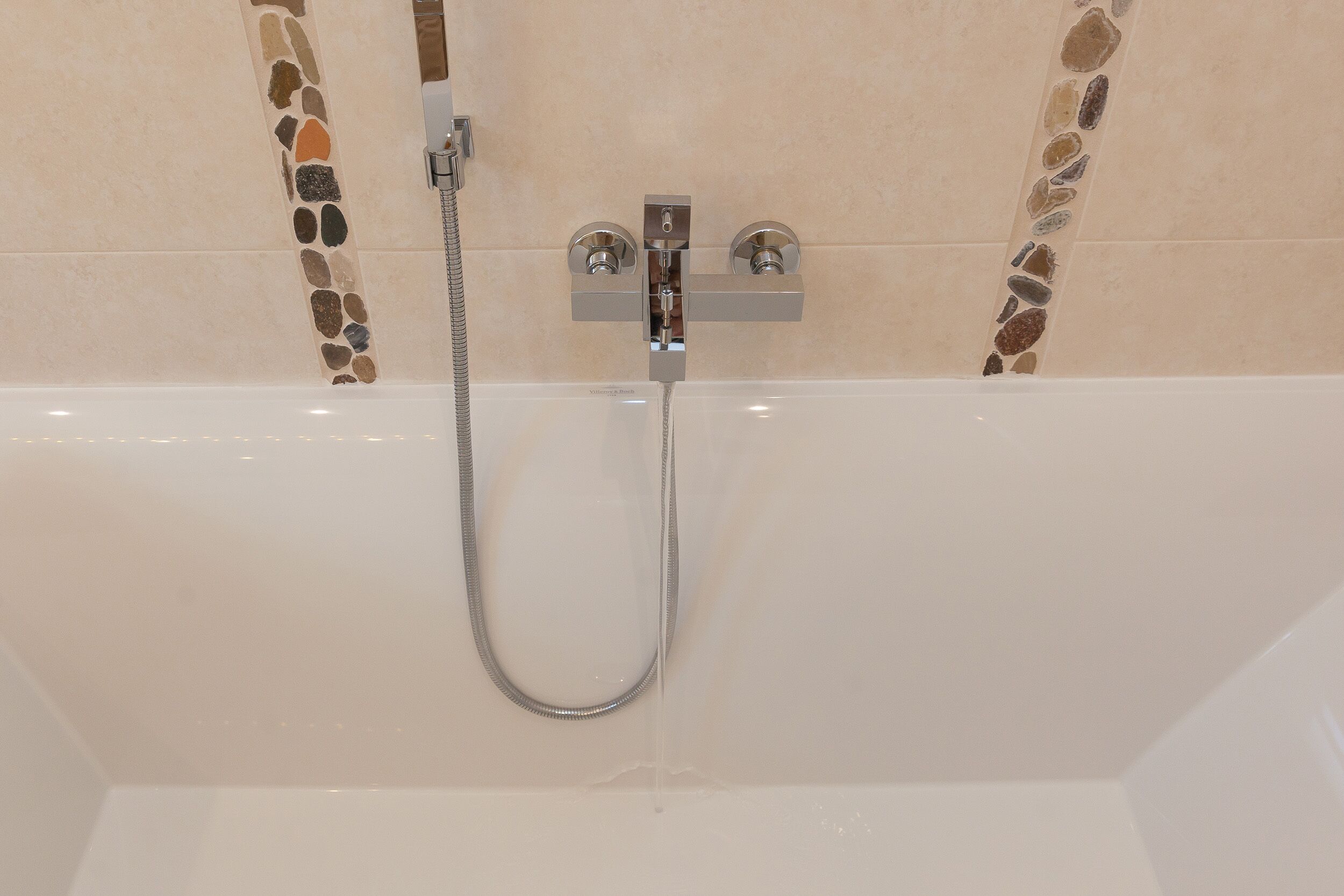A shower with a handheld hose and a wall-mounted control panel.