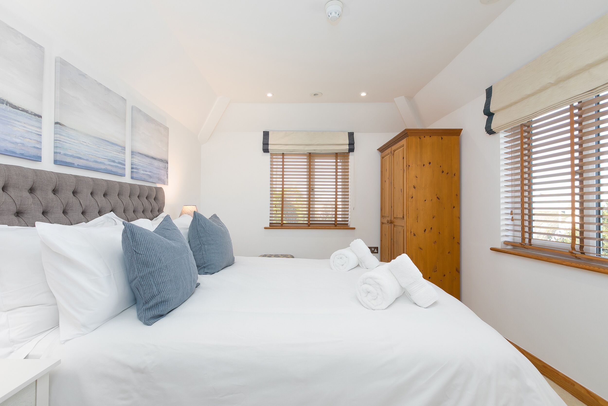 A bedroom with a large bed, a headboard, a wardrobe, and a window with blinds.