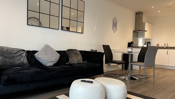 A modern living room with a black sofa, two ottomans, a striped rug, and a dining area with chairs and a table.
