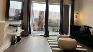 A modern living room with a flat-screen TV, a sofa, a coffee table, and a sliding glass door leading to a balcony.