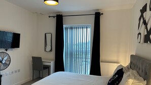 A hotel room with a bed, a desk, a chair, a TV, and a window with curtains.