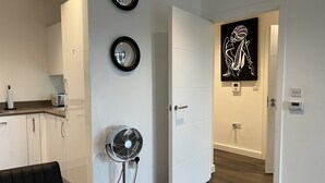 A modern kitchen with white cabinets, a black-framed mirror, a standing fan, and a black artwork on the wall.