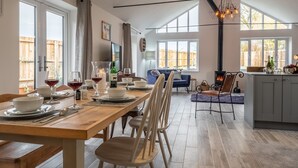 A spacious dining area with a wooden table set for a meal, a kitchen with a stove, and a cozy seating area with a blue sofa and a fireplace. - Weavers, Felbrigg, Norfolk (Felbrigg)