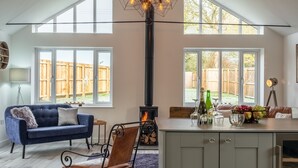 A spacious living room with a fireplace, a sofa, a dining area, and large windows. - Weavers, Felbrigg, Norfolk (Felbrigg)