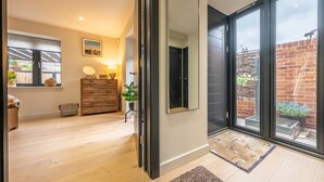 Ein modernes Interieur mit Holzboden, einer schwarzen Schiebetür und Blick auf eine Ziegelwand und einen Garten durch große Fenster.
