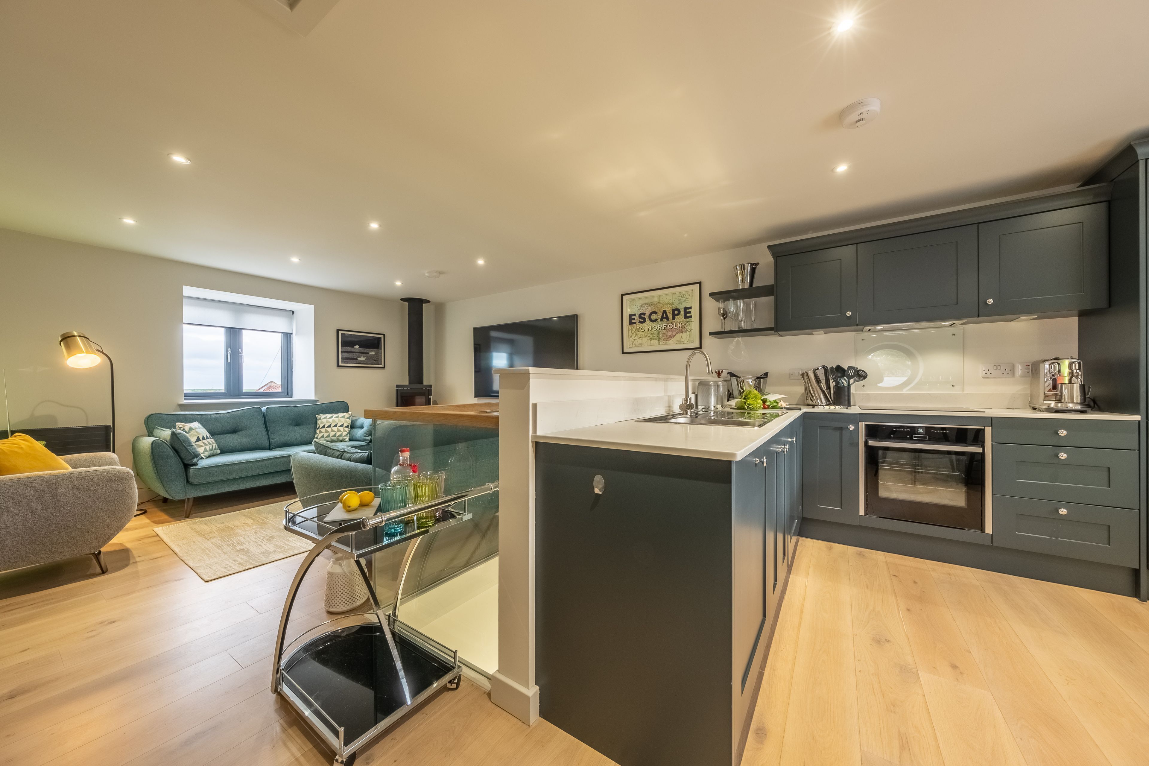 A modern kitchen with dark cabinets, a built-in oven, and a dining area with a glass table and chairs.