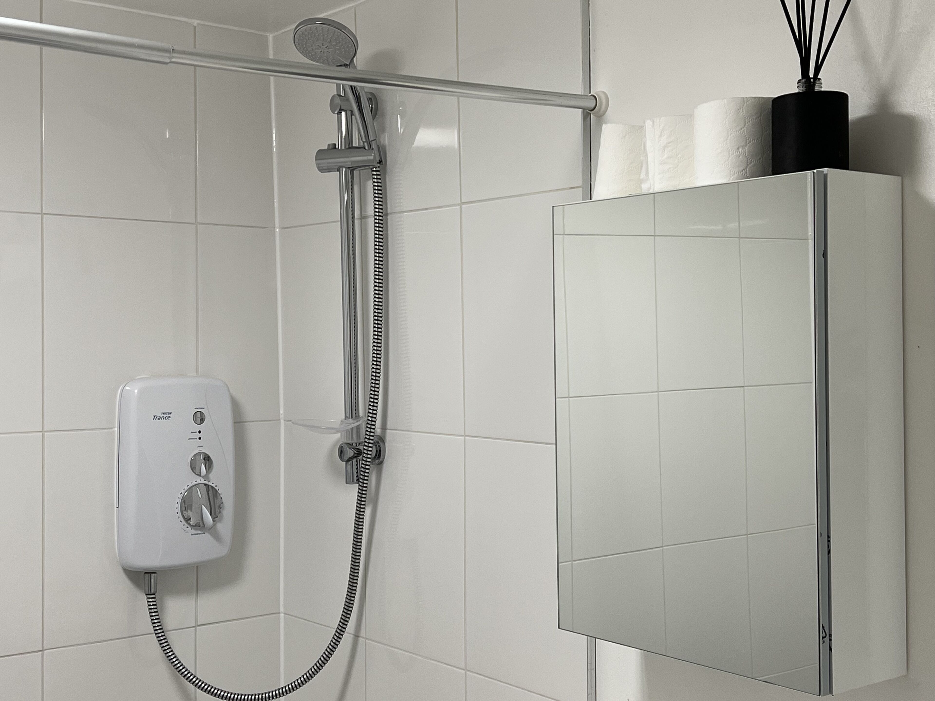 Une douche équipée d’un pommeau de douche à main, d’un flexible de douche et d’un panneau de commande.