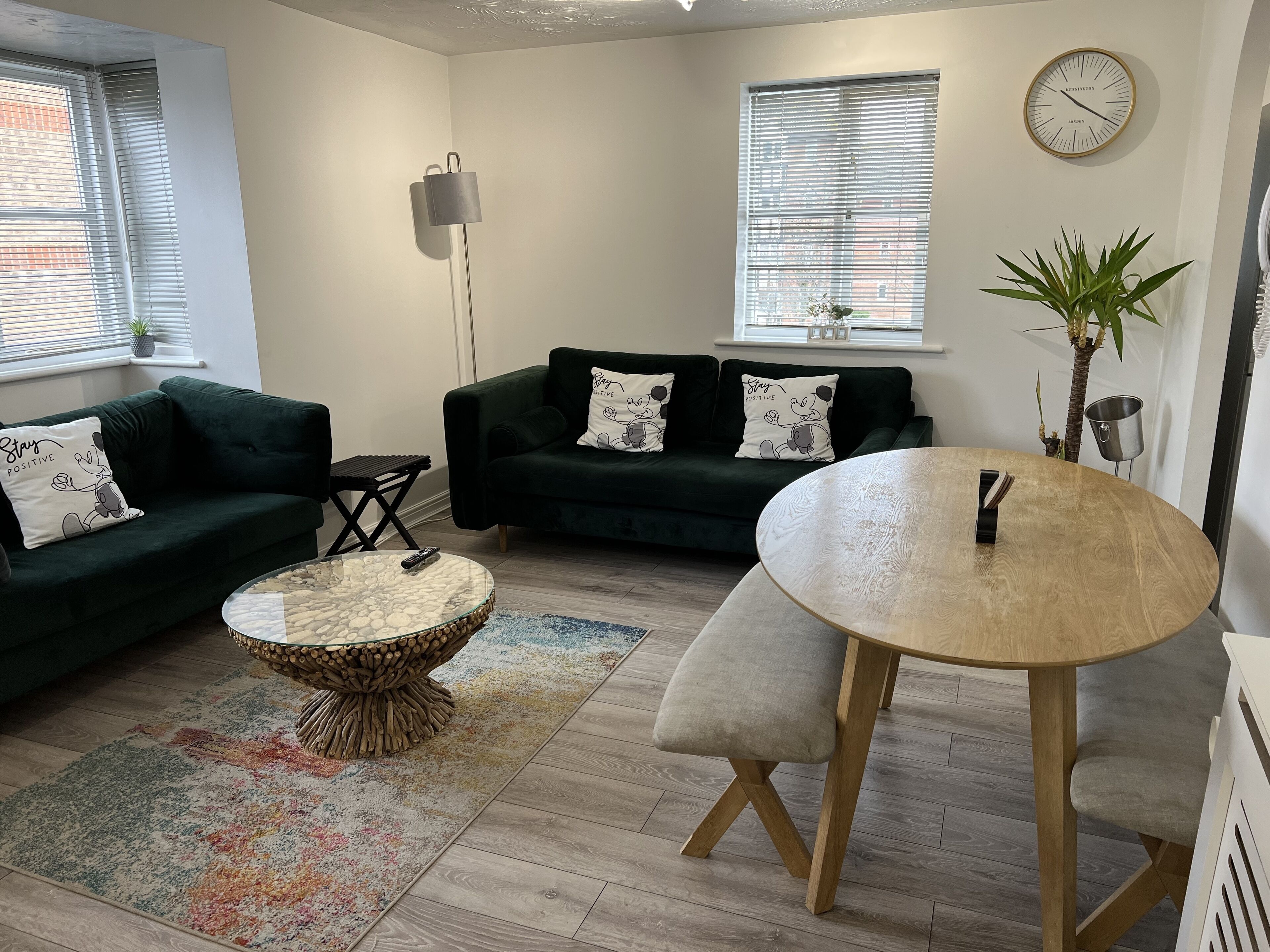 A modern living room with two dark green sofas, a round coffee table, a small side table, and a dining table with a bench.