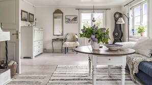A room with a white dresser, a chair, a table with a vase of flowers, a sofa, and a window with a view. - 4 bedroom cozy home in Ellös (Ellös)