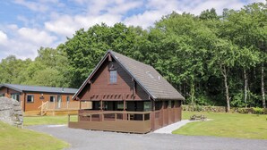 A wooden cabin with a porch, surrounded by a well-maintained lawn and trees. - Moyle Lodge (Dalbeattie)