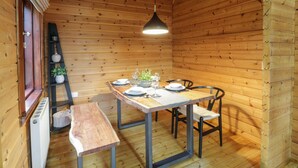A wooden interior with a dining table set for four, a bench, and a ladder shelf with decorative items. - Moyle Lodge (Dalbeattie)