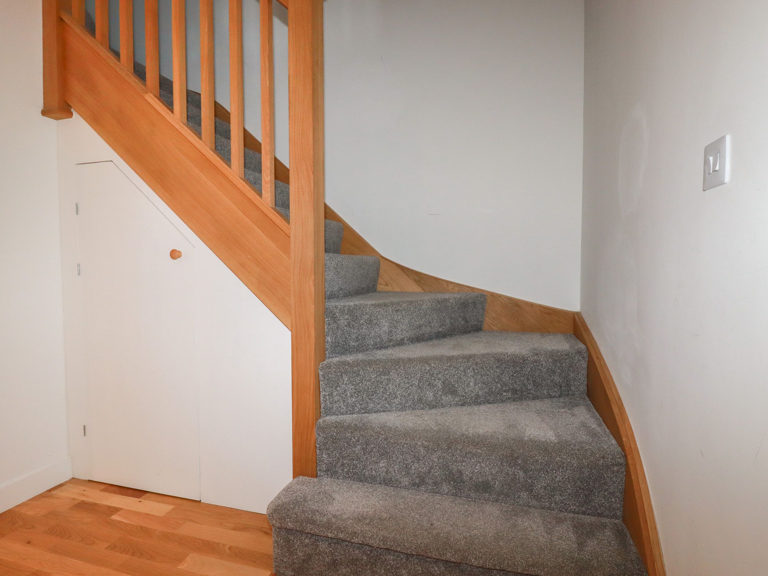 A staircase with wooden railings and carpeted steps leading to a door.