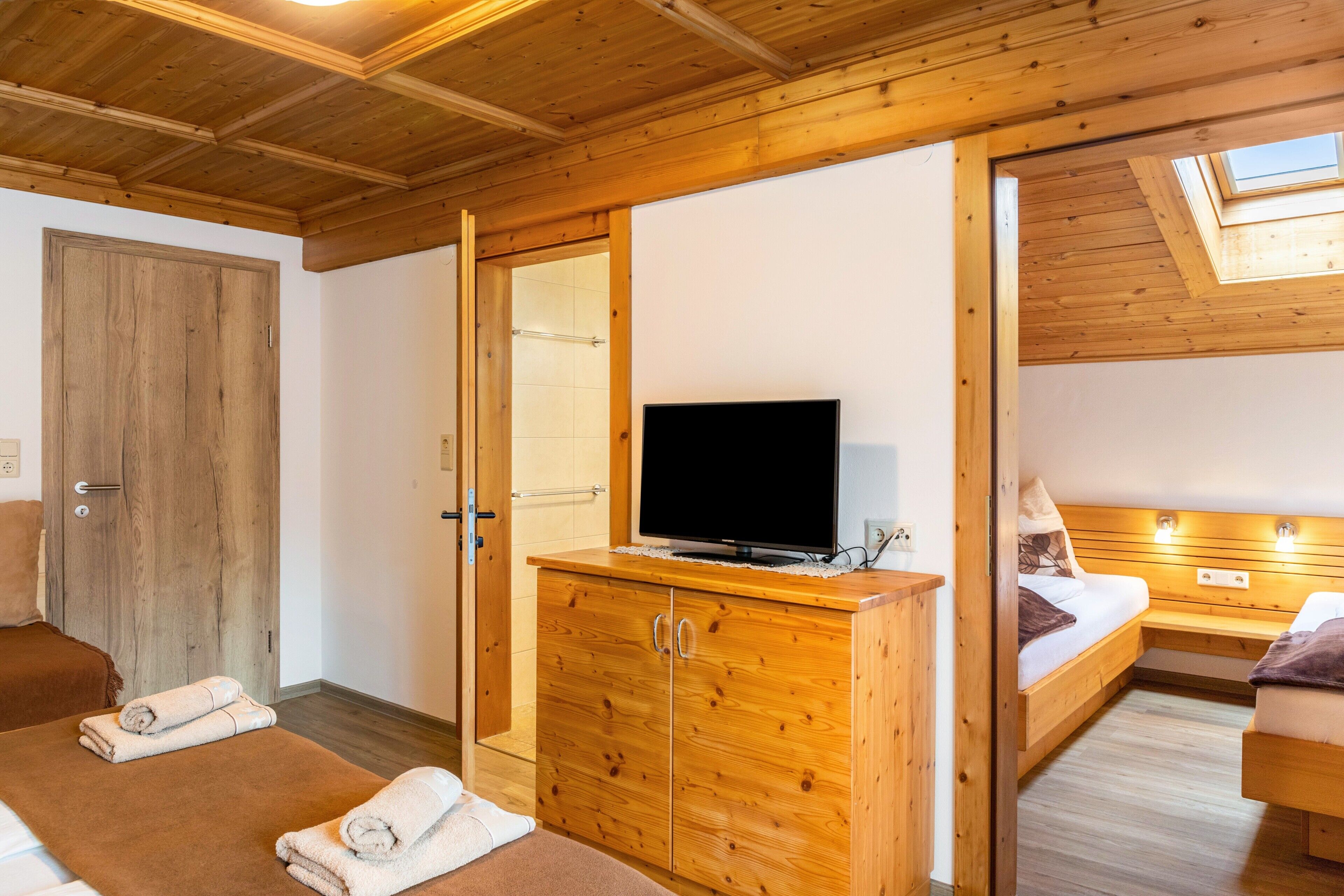 Interno di una baita di legno con una TV su una cassettiera, un letto e un bagno con porta in legno.
