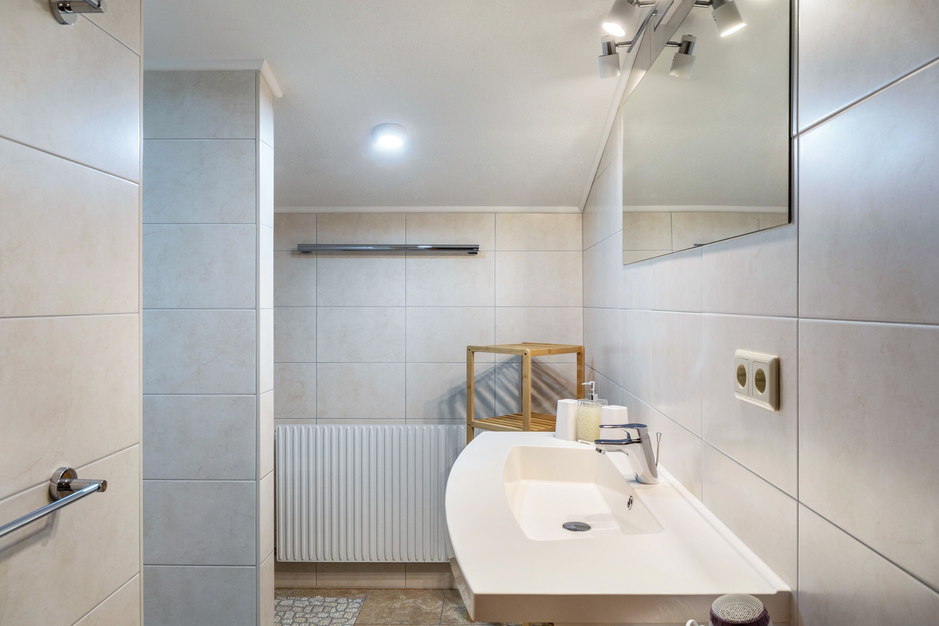 Une salle de bain moderne avec un lavabo blanc, un miroir, un porte-serviettes et un radiateur.