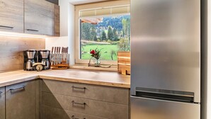 A kitchen with a stainless steel refrigerator, wooden cabinets, a coffee maker, and a window with a view of a green landscape. - Apartment Catrin – Hochzillertal/Hochfügen Ski Area, Sauna, EV Charging, Mountain Views (Ried im Zillertal)