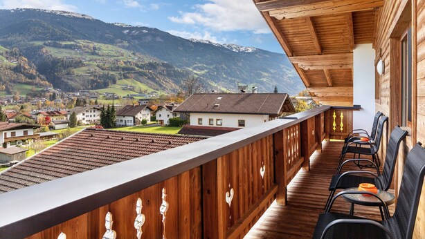 A wooden balcony with chairs, overlooking a village and mountains. - Apartment Catrin – Hochzillertal/Hochfügen Ski Area, Sauna, EV Charging, Mountain Views (Ried im Zillertal)