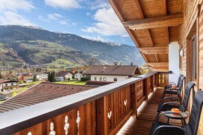 Ein Holzbalkon mit Stühlen, mit Blick auf ein Dorf und Berge.