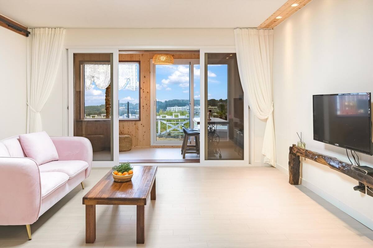 A modern living room with a pink sofa, a wooden coffee table, and a TV on a wooden stand.