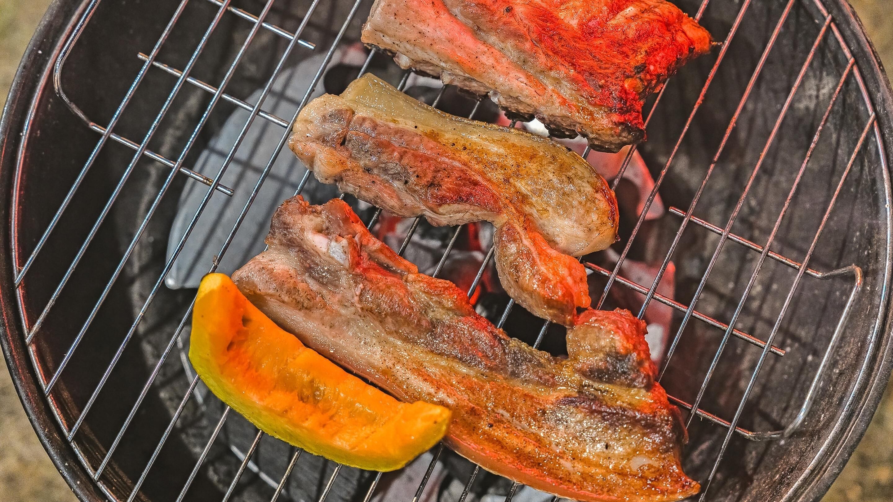 A grill with several pieces of meat and a slice of yellow bell pepper.