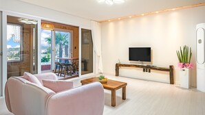 Una sala de estar moderna con un sofá, una mesa de centro con fruta, un televisor montado en la pared y vistas a palmeras a través de la puerta de vidrio.