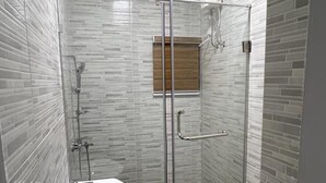 Een moderne badkamer met een douchecabine van glas, een wit wastafelmeubel en een houten raam.