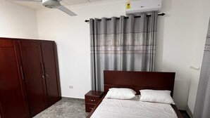 Een slaapkamer met een bed, een kledingkast, een plafondventilator en een raam met gordijnen.