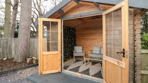 A wooden cabin with an open door, a bench inside, and a Christmas tree.
