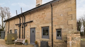 A stone building with a grey door, windows, and a bench outside.