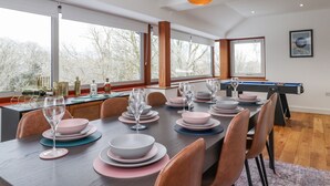 Un espace repas avec une table de billard, de grandes fenêtres et une vue sur les arbres.