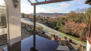 Un espace extérieur aménagé, abrité et doté d’une table et de chaises, offrant une vue panoramique sur un paysage pittoresque avec des collines et une étendue d’eau.
