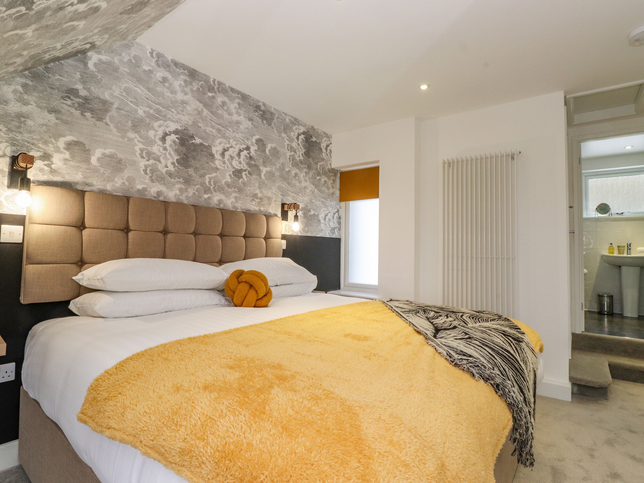 A modern bedroom with a tufted headboard, a large bed with white and yellow bedding, and a textured ceiling.