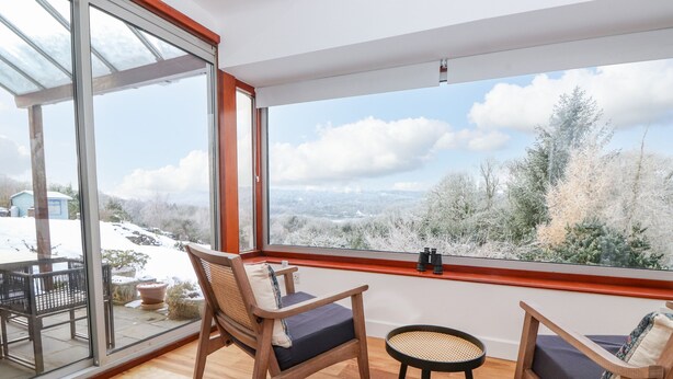 Un balcon avec des chaises en bois et une petite table, de grandes fenêtres donnant sur un paysage enneigé.