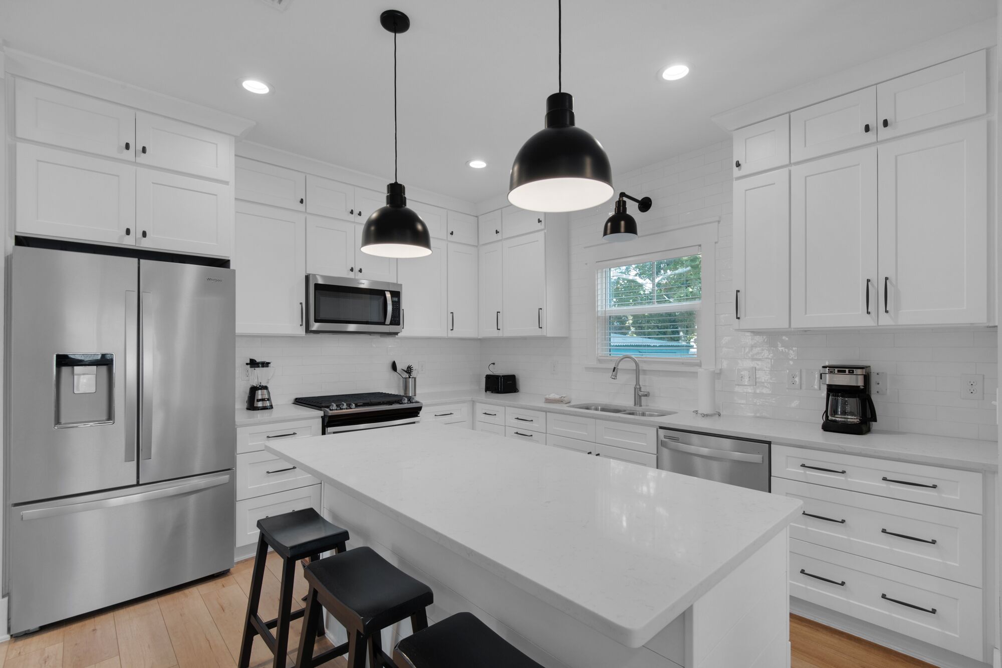 A modern kitchen with white cabinetry, stainless steel appliances, a central island with bar stools, and pendant lighting.