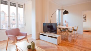 Uma sala de estar moderna com televisão, um espaço de refeições e uma grande janela com vista para edifícios.