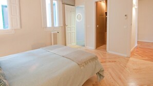 Quarto com cama, radiador, janela e porta que dá para outro cômodo.