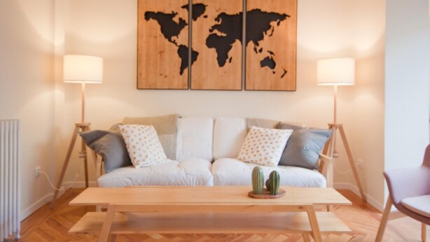 Uma sala de estar com piso de madeira, um sofá com almofadas estampadas, uma mesa de centro e uma obra de arte com um mapa-múndi acima do sofá.