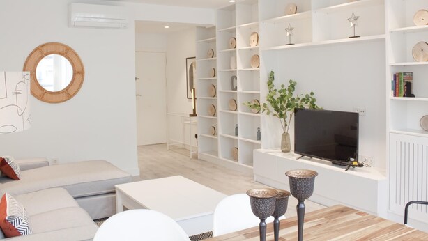 A modern living room with a sofa, coffee table, and TV stand. There are shelves with decorative items and a mirror on the wall. - Brand new 2 bedroom apartment by RIO 2 and Matadero (Madrid)