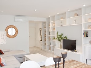 A modern living room with a sofa, coffee table, and TV stand. There are shelves with decorative items and a mirror on the wall.